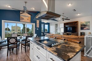 A modern kitchen with a large island, dining area with chairs, a sofa, and a TV in a living room. - Coastal Canary - Hot tub, beach, fire pit (Flagler Beach)