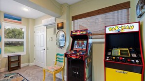 Huoneessa on Pac-Man-peliautomaatti, tuoli, pieni pöytä ja ikkuna, jossa on sälekaihtimet.