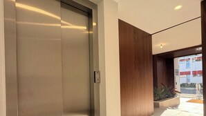 Un ascensor moderno con detalles metálicos, una pared blanca impecable y un panel de madera a la derecha.
