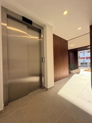 A modern elevator with a metallic finish, a clean white wall, and a wooden panel on the right. - Entrecubos Apartments - Olhão City Center (Olhão)