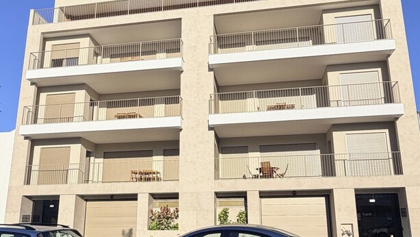Un edificio de varios pisos con balcones, una entrada de garaje y un coche estacionado al frente.