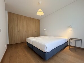 A bedroom with a bed, a wardrobe, a bedside table, and a hanging light fixture. - Entrecubos Apartments - Olhão City Center (Olhão)