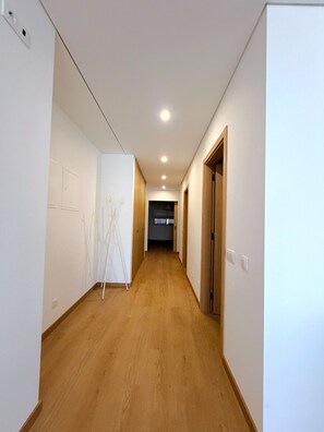 A narrow hallway with wooden flooring, white walls, and recessed ceiling lights. - Entrecubos Apartments - Olhão City Center (Olhão)