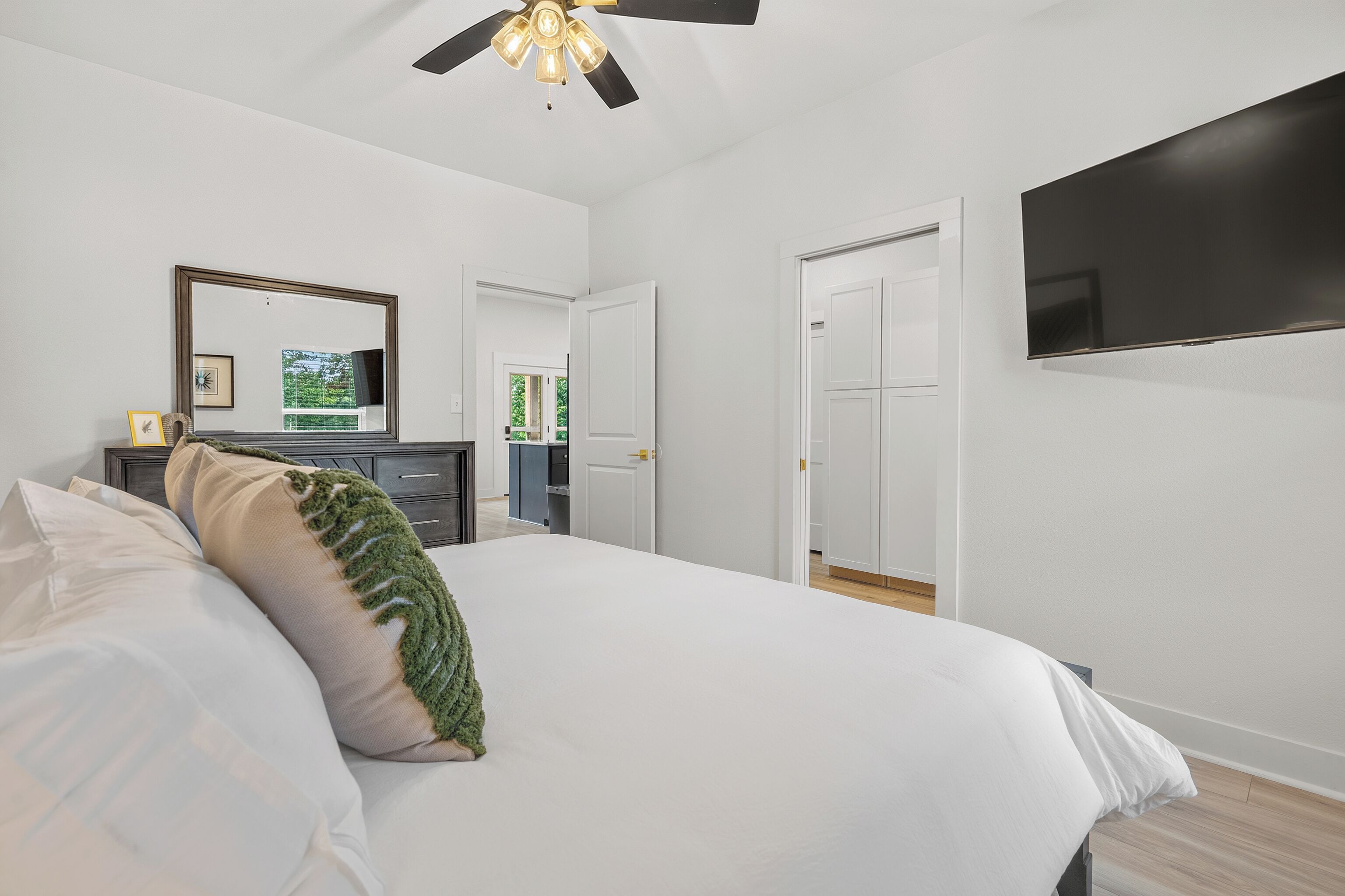 A bedroom with a bed, a television, a ceiling fan, and a door.
