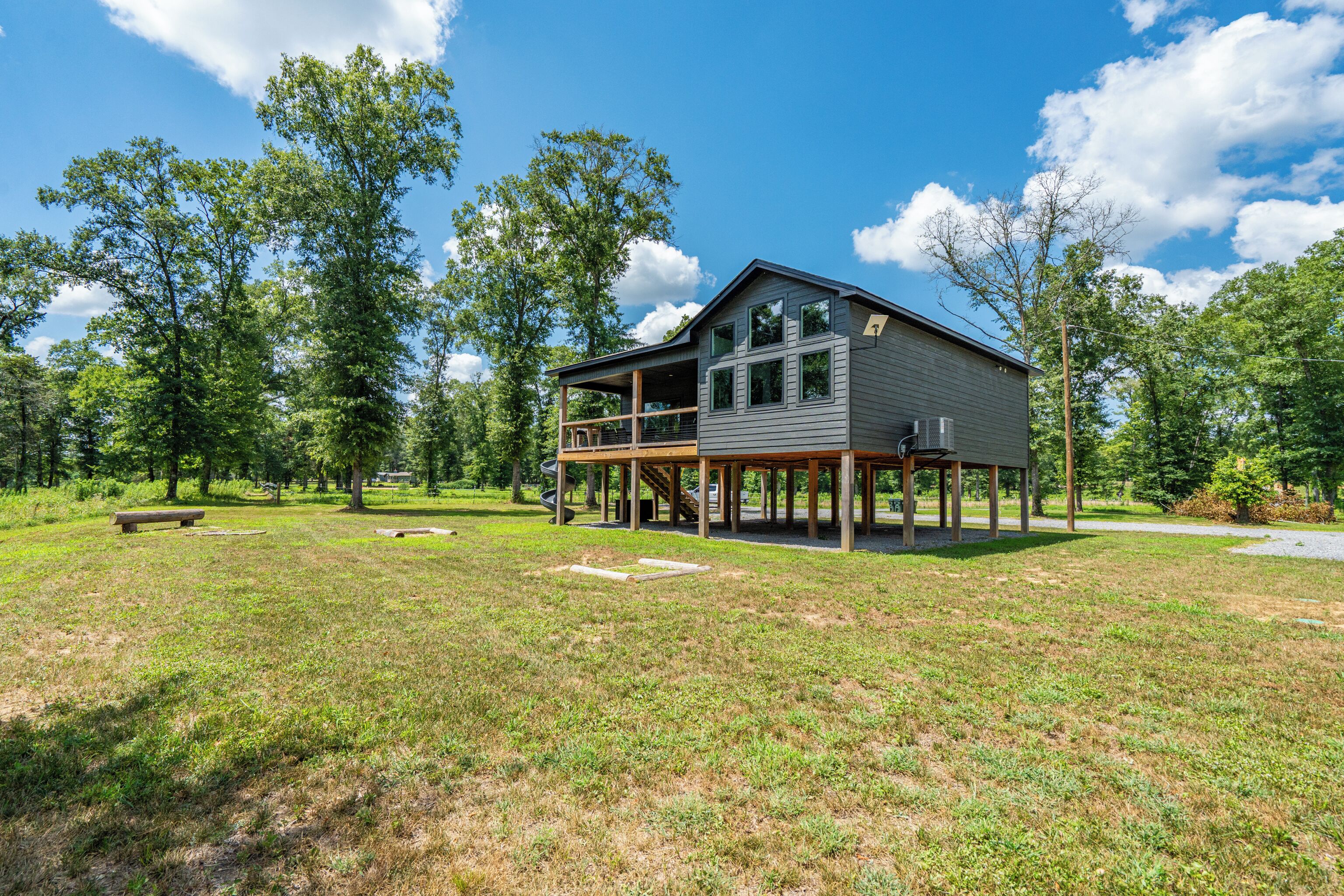 A two-story house with a deck, surrounded by a grassy yard and trees.