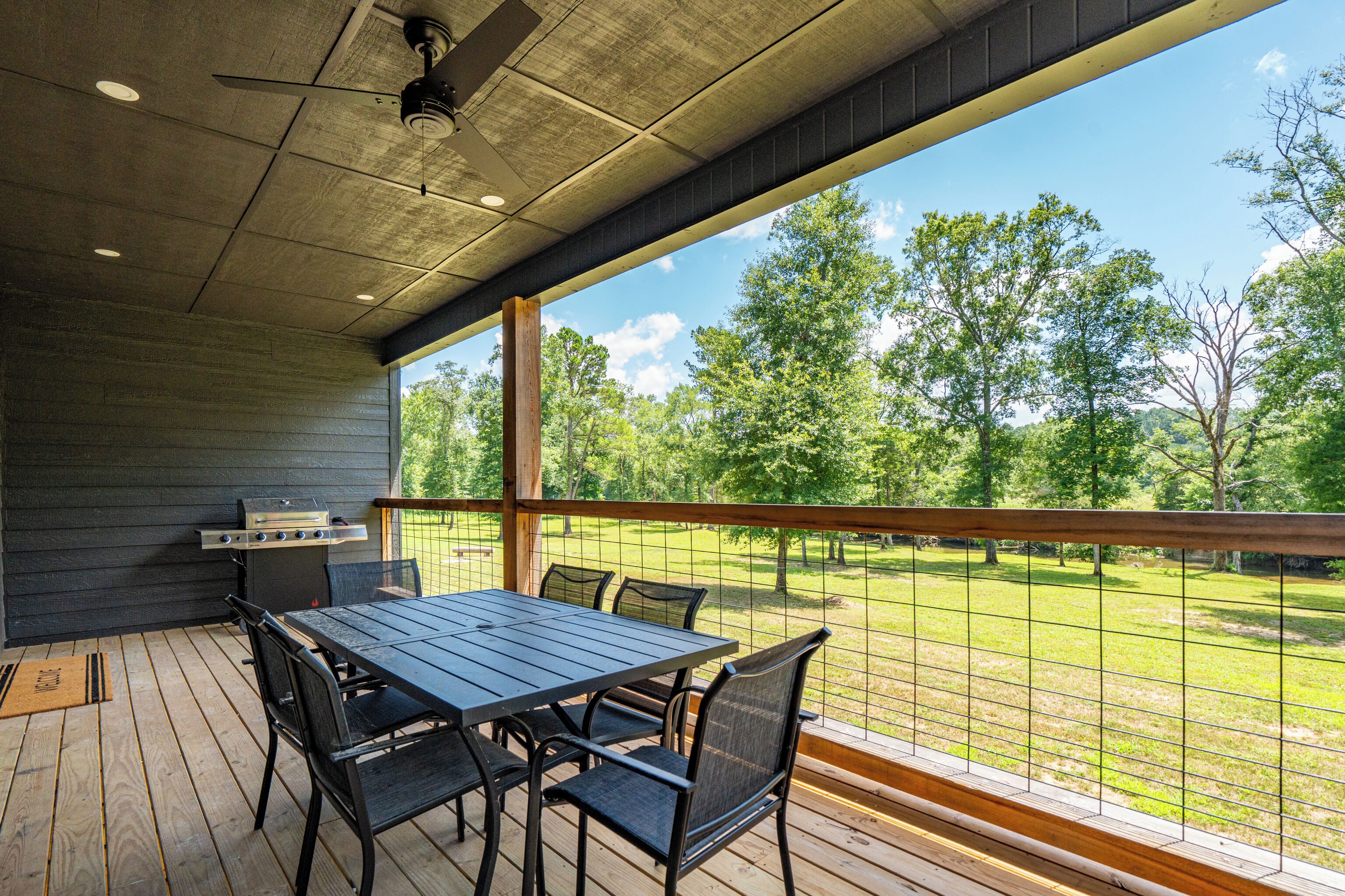 An outdoor patio with a table and chairs, a grill, and a view of a grassy area with trees.