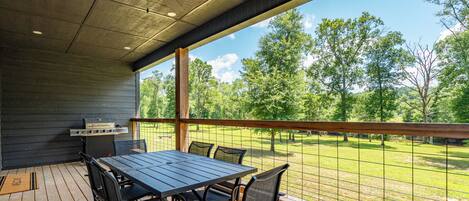 An outdoor patio with a table and chairs, a grill, and a view of a grassy area with trees.