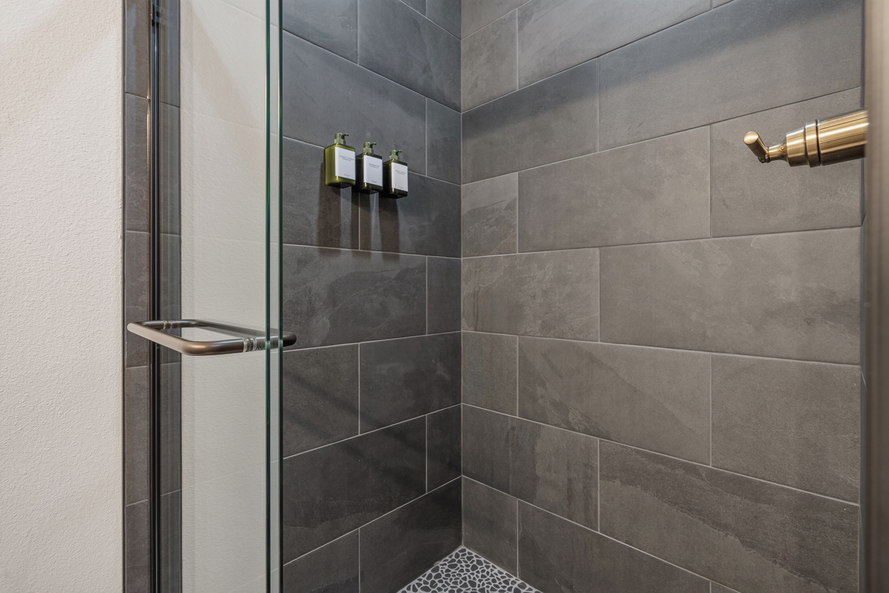 A shower with dark tiles, a glass door, and a towel rack.