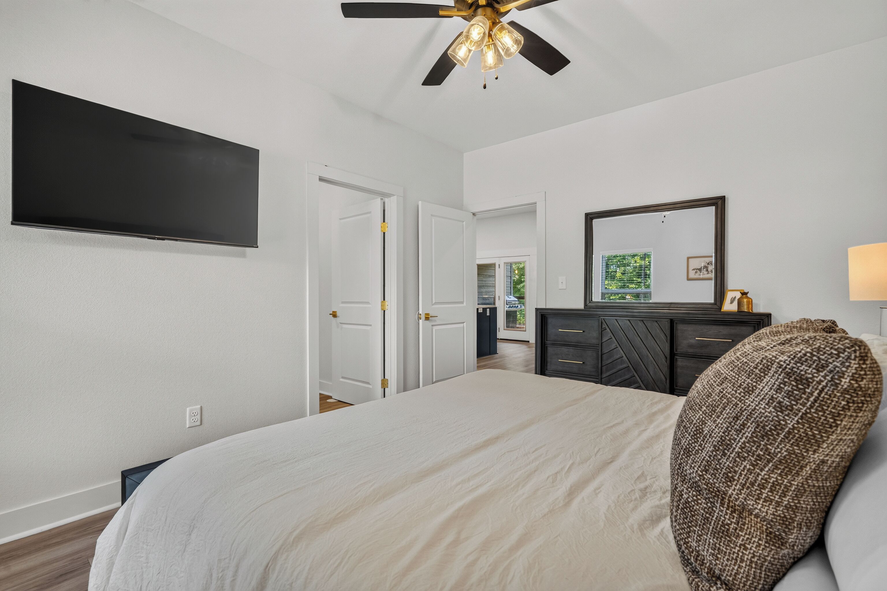A bedroom with a bed, a flat-screen TV, a ceiling fan, a dresser, and a mirror.