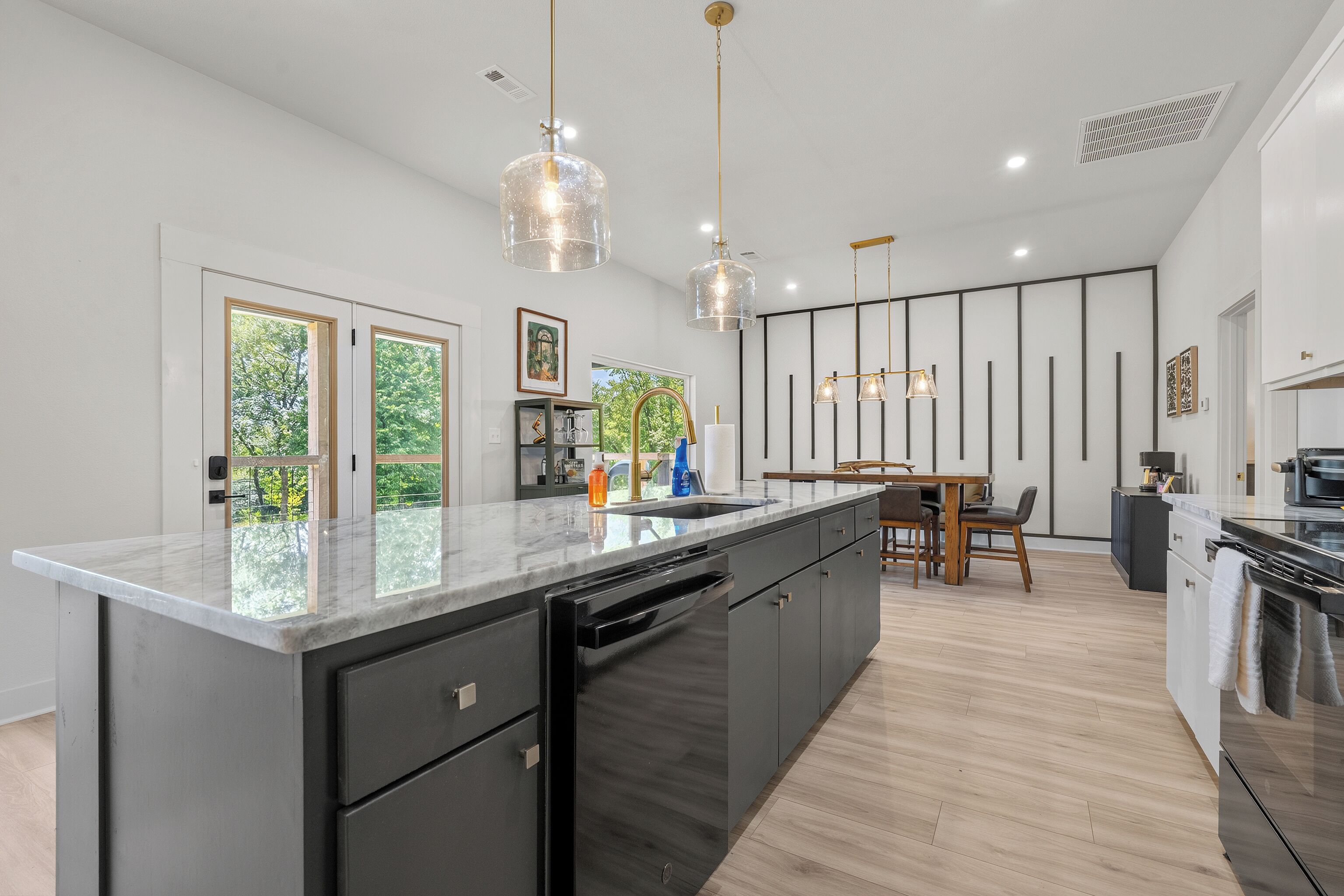 A modern kitchen with a large island, black cabinetry, and pendant lighting.
