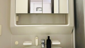 Un baño con un lavamanos blanco, un espejo encima y una puerta con ventanal.