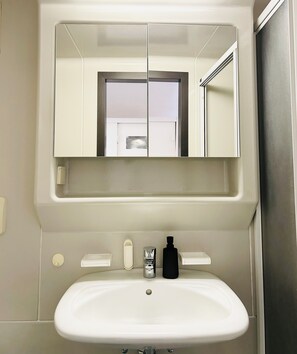 Un baño con un lavamanos blanco, un espejo encima y una puerta con ventanal.