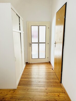 Un pasillo con suelo de madera, una puerta blanca con paneles de vidrio esmerilado y un armario blanco a la izquierda.