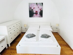 A neatly arranged bedroom with a bed, two bedside tables, a dresser, and a wall-mounted picture of flowers.