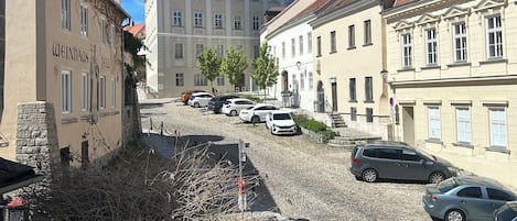 A cobblestone street lined with historic buildings, parked cars, and a clear blue sky.