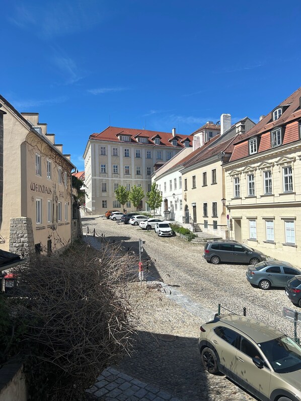 A cobblestone street lined with historic buildings, parked cars, and a clear blue sky.