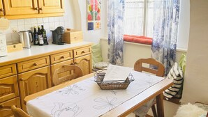 Un comedor con una mesa, sillas, armarios de madera, un ventanal con cortinas y una pared decorada con obras de arte.