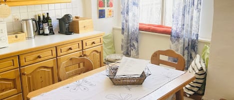 Un espace repas comprenant une table, des chaises, des meubles en bois, une fenêtre avec des rideaux et un mur décoré d’œuvres d’art.