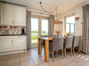 A kitchen with a dining area, featuring a table with chairs, a coffee machine, and a view of the outdoors. - 6-guest Texel Villa With Sauna & Spa (De Koog)