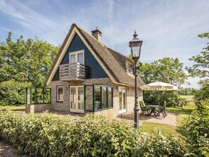 A house with a thatched roof, a balcony, and a garden with a table and chairs. - 6-guest Texel Villa With Sauna & Spa (De Koog)