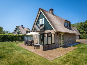 A traditional house with a thatched roof, a stone extension, and a patio with outdoor furniture. - 6-guest Texel Villa With Sauna & Spa (De Koog)