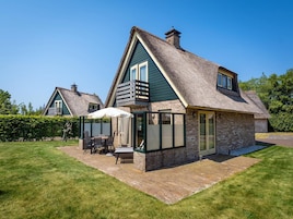 A traditional house with a thatched roof, a stone extension, and a patio with outdoor furniture.