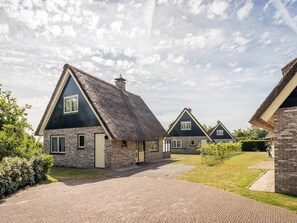 A row of houses with a brick facade and dark roofs, set in a sunny, grassy area. - 6-guest Texel Villa With Sauna & Spa (De Koog)