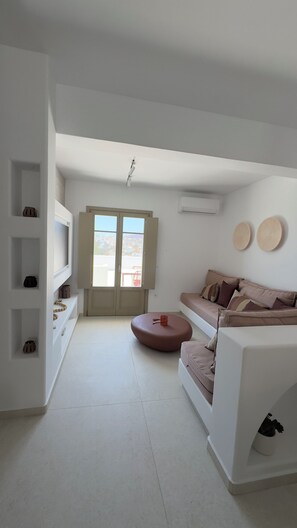 A modern living room with a sofa, a TV, a window, and a ceiling fan. - Borgo Stampalia – Villa Terracotta (Astypalea)