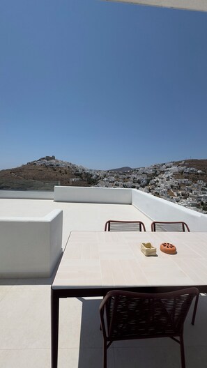 Eine Dachterrasse mit Tisch und Stühlen, mit Blick auf eine Hügelside mit weißen Gebäuden.