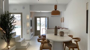 A modern dining area with a round table, wooden chairs, and a pendant light. - Borgo Stampalia – Villa Terracotta (Astypalea)