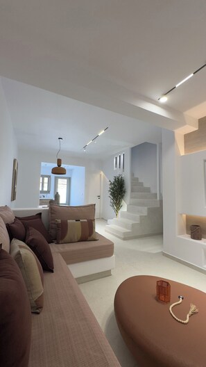 A modern living room with a sofa, a coffee table, and a staircase leading to an upper level. - Borgo Stampalia – Villa Terracotta (Astypalea)