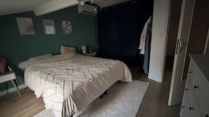 Ein Schlafzimmer mit einem Bett, einem Schminktisch, einem Nachttisch und einem Fenster mit Vorhängen.
