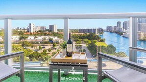 Een balkon met een tafel, twee stoelen, een fles wijn en een glas. Achtergrond toont een stadsbeeld en een rivier.
