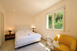 Ein Schlafzimmer mit einem Bett, Nachttischen, einem Fenster mit Blick und einem gelben Sessel.
