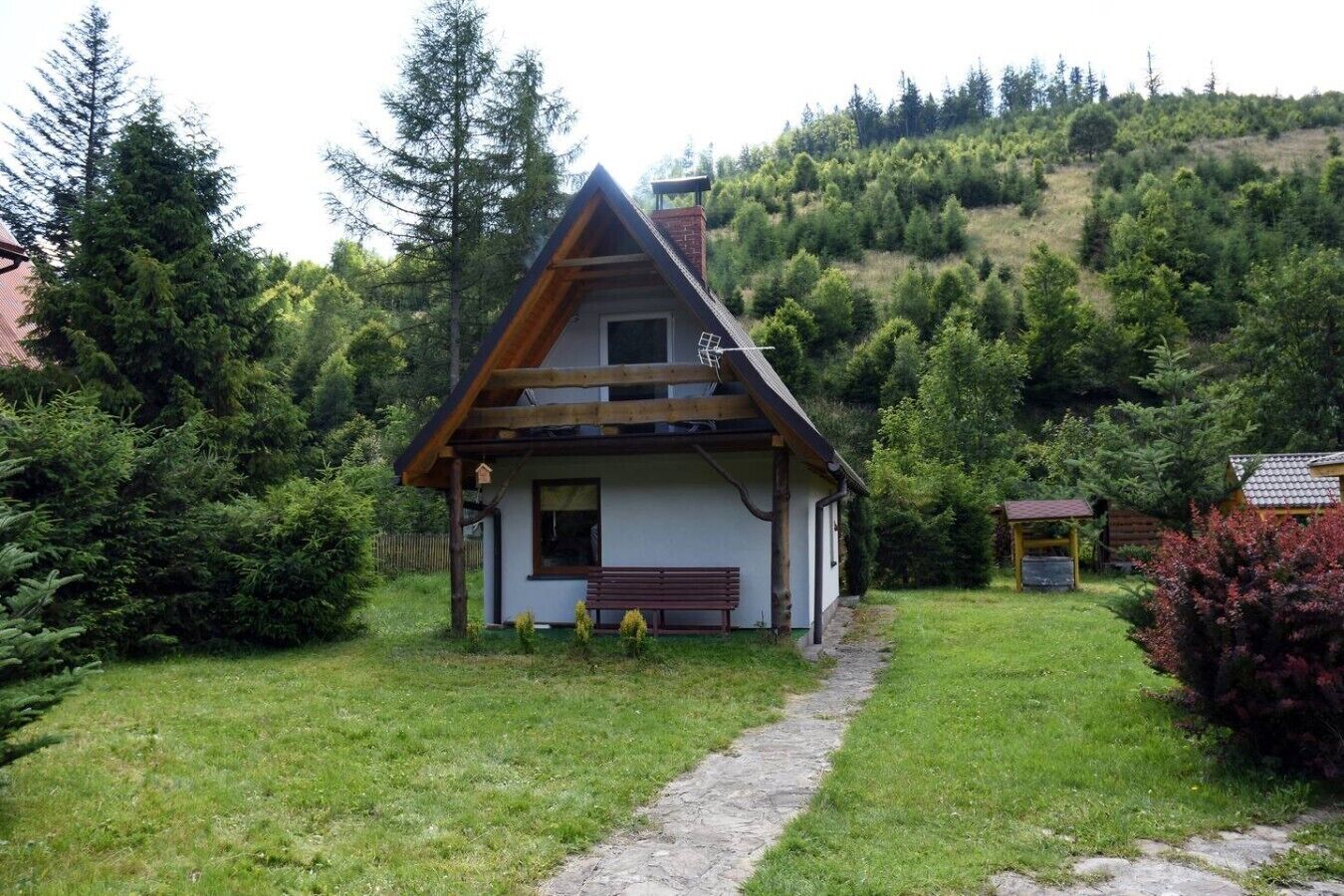 Een klein huis met een schuin dak, een houten veranda en een pad van stenen dat er naartoe leidt.