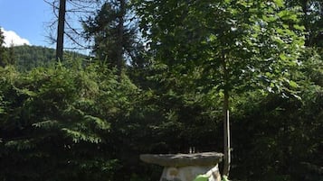A pair of green cushioned lounge chairs in a grassy outdoor area with a backdrop of trees and a clear sky.