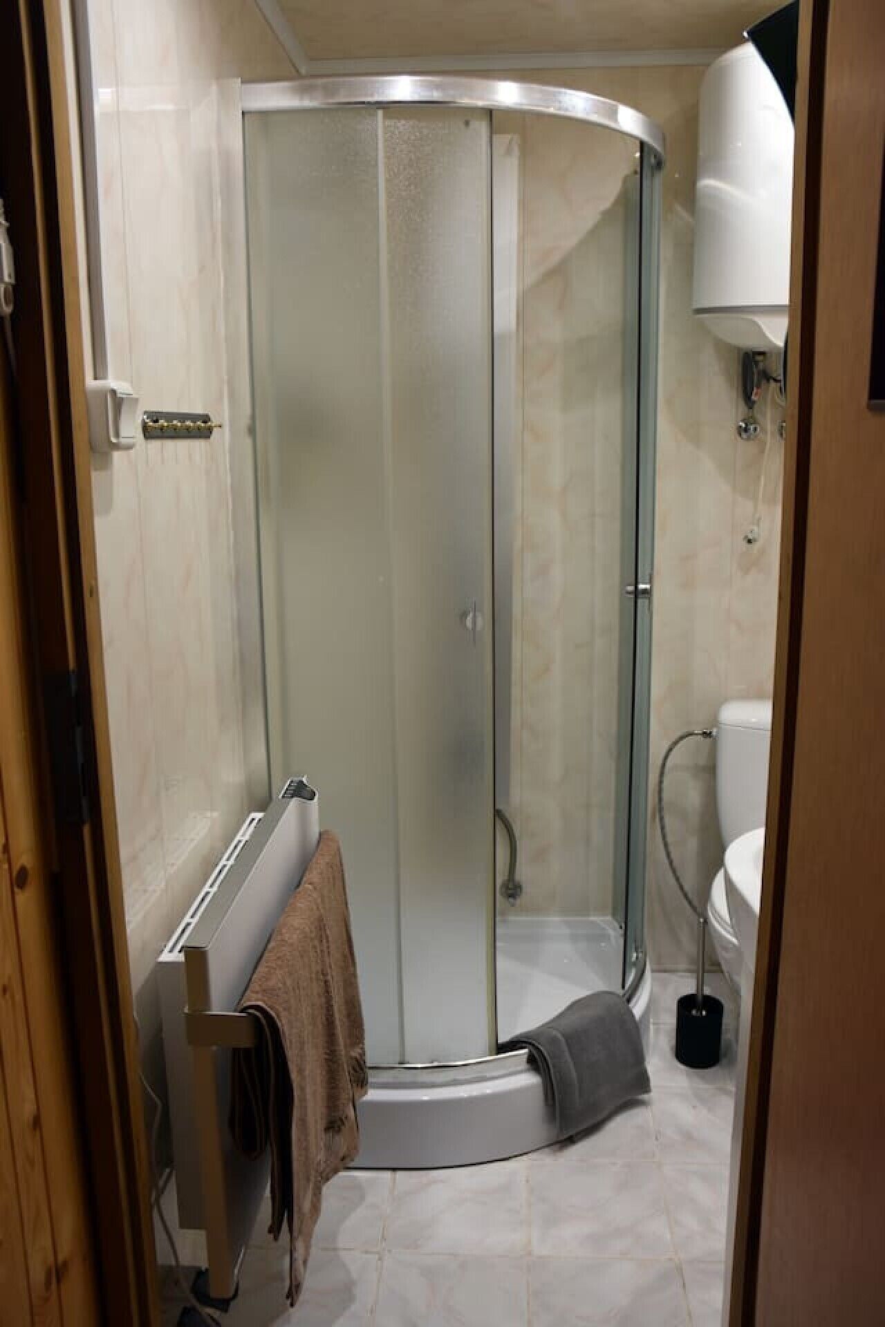 Una dutxa amb porta de vidre, un penjallat de tovalloles i un vàter al bany.