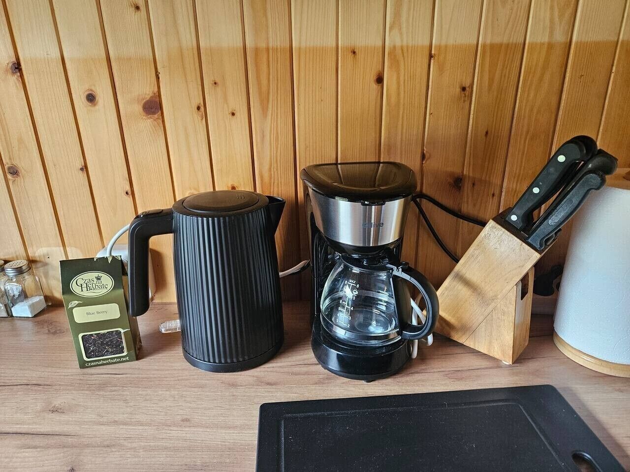 Keittiön työtasolla on kahvinkeitin, vedenkeitin, veitsiteline ja paketti kahvipapuja.