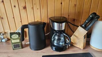 Keittiön työtasolla on kahvinkeitin, vedenkeitin, veitsiteline ja paketti kahvipapuja.