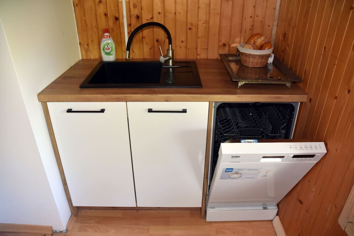 Een kleine keuken met een spoelbak, twee kastjes en een vaatwasser.