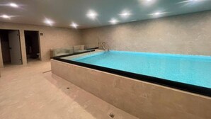 A swimming pool with a glass enclosure, a ladder, and a tiled floor. - Mexican Designer Studio - Pool, Gym, and Rooftop (Ciudad de México)