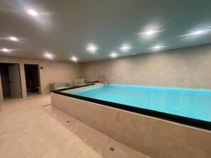 A swimming pool with a glass enclosure, a ladder, and a tiled floor. - Mexican Designer Studio - Pool, Gym, and Rooftop (Ciudad de México)