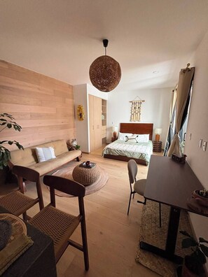A modern bedroom with a wooden headboard bed, a sitting area with a sofa and chairs, a dining table, and a hanging light fixture. - Mexican Designer Studio - Pool, Gym, and Rooftop (Ciudad de México)