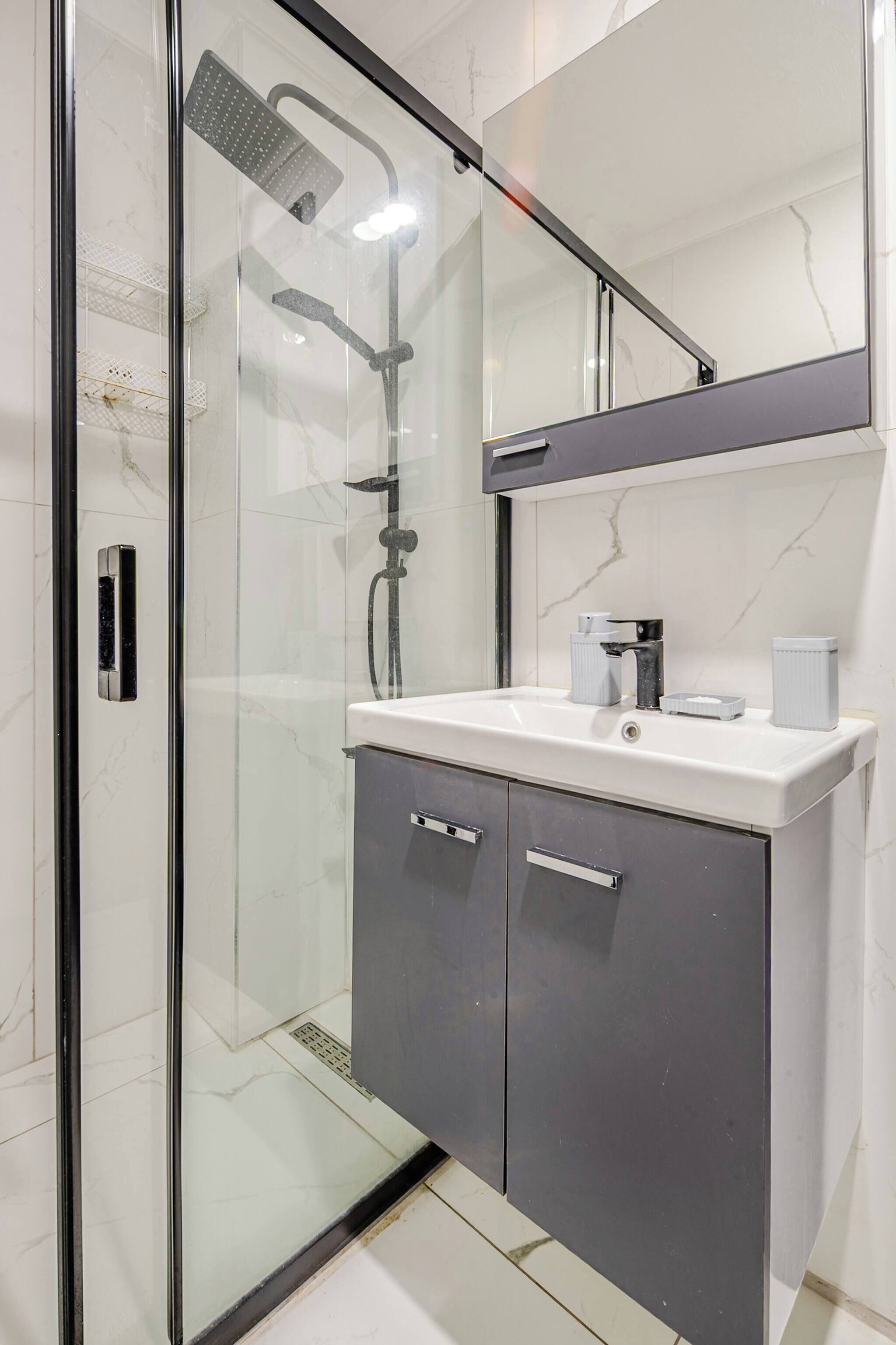 Une salle de bain moderne avec une douche à parois de verre, un lavabo blanc et un meuble aux tons foncés.