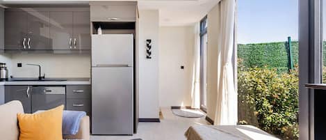 Une chambre moderne comprenant un canapé, un lit, une petite table, un coin cuisine et une grande fenêtre donnant sur un paysage verdoyant.