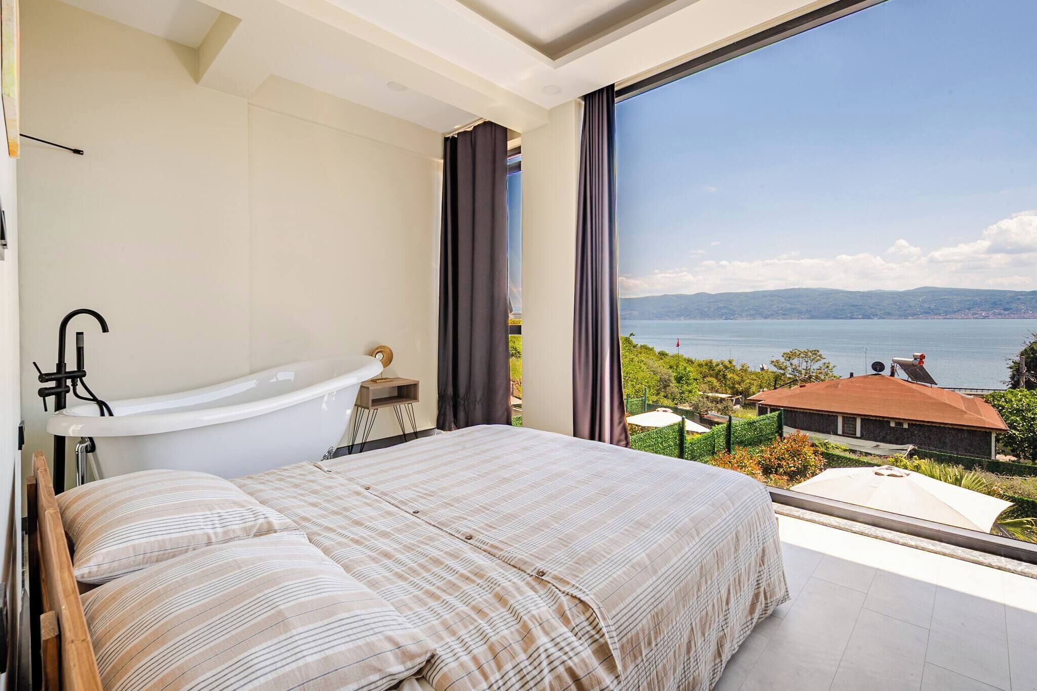 A bedroom with a large bed, a bathtub, and a view of the sea.