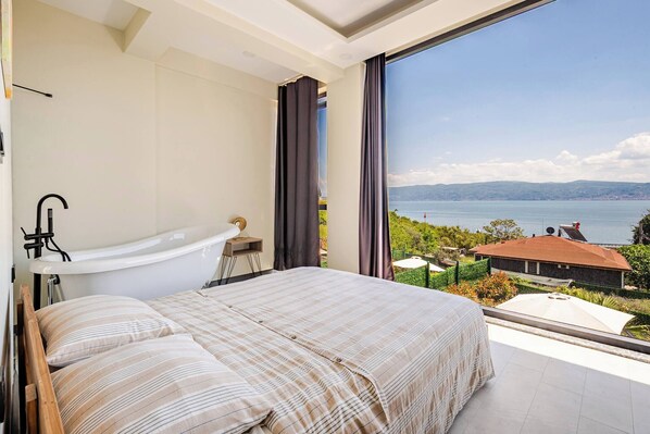 A bedroom with a large bed, a bathtub, and a view of the sea.
