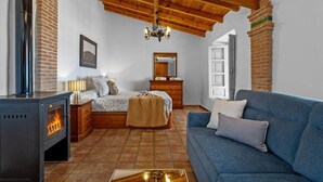 Ein gemütliches Zimmer mit Kaminofen, einem Bett, einer Kommode, einem Spiegel und einem blauen Sofa.