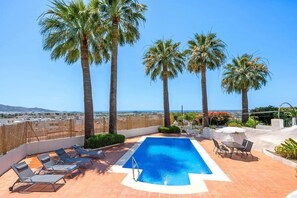A rooftop pool with palm trees, a view of the city, and a clear sky.