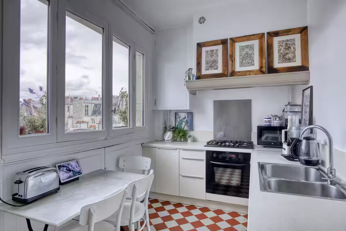 A kitchen with a stove, oven, microwave, and sink. There are framed pictures on the wall and a window with a view of buildings outside.